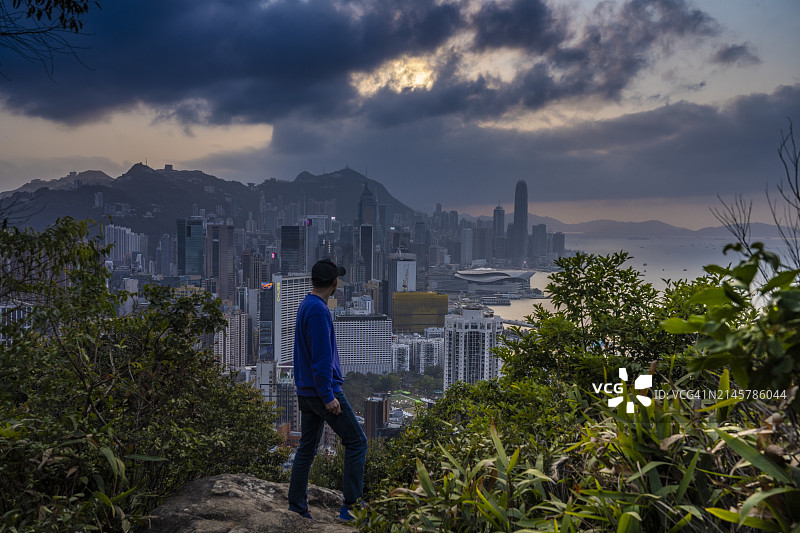 亚洲人站在岩石上看香港的天际线，日落图片素材