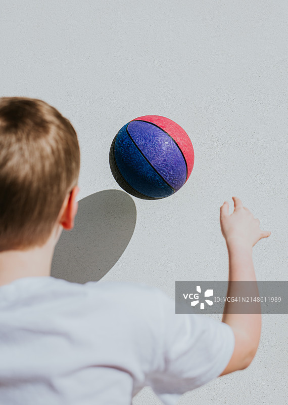 一个年轻的小伙子对着白色的墙投掷并接住了一个彩色的篮球图片素材