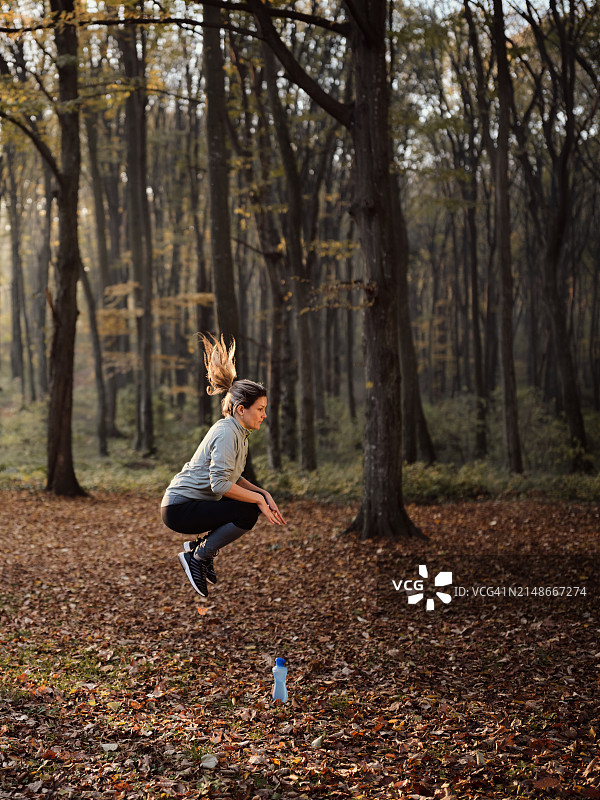 秋天的一天，女运动员在树林里练习跳跃。图片素材