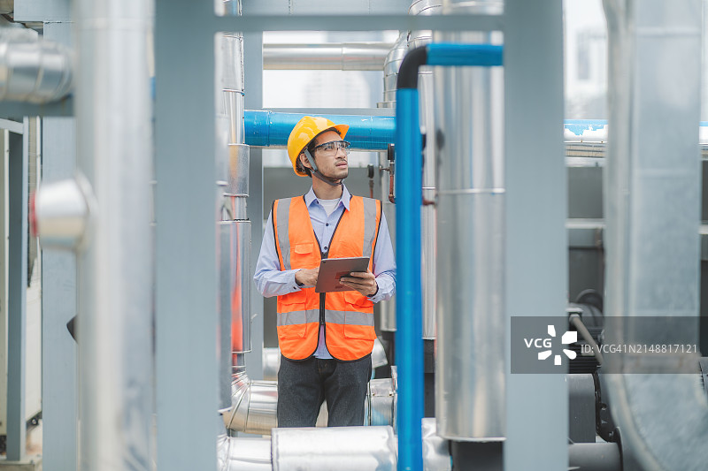 工人戴安全帽，穿安全背心，在工业设施检查机械夹板。图片素材