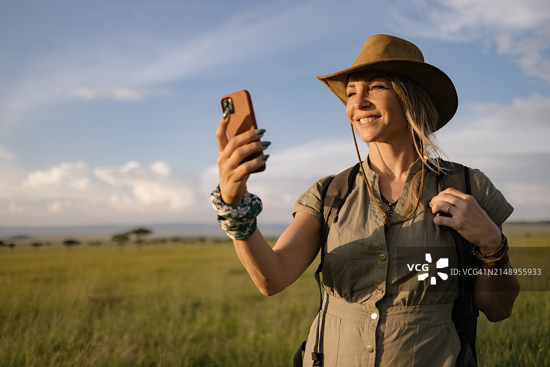 快乐的女探险家在野生动物保护区使用智能手机。图片素材