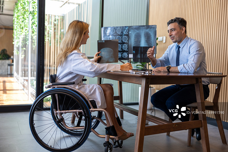 包容性医疗:坐在轮椅上的残疾女医生为男病人提供富有同情心的医疗服务图片素材
