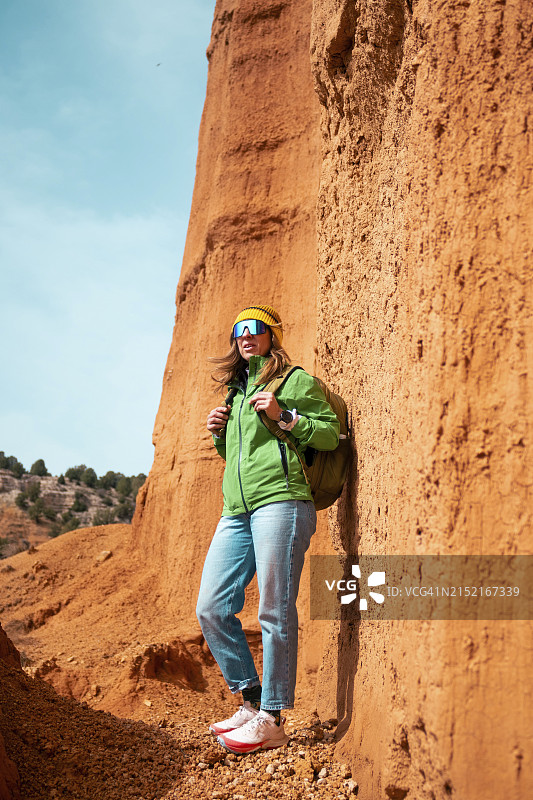 在阳光明媚的日子里，一个成熟的女人背着背包站在峡谷的红色悬崖边图片素材