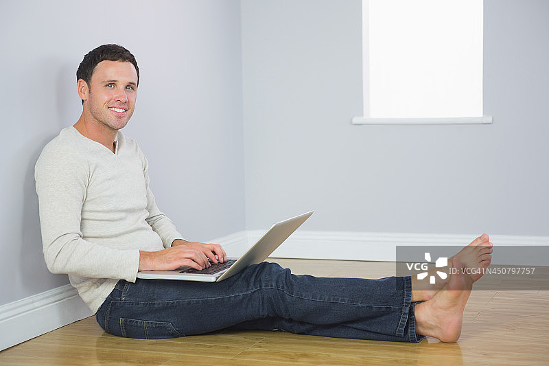一个漫不经心的微笑着靠在墙上用笔记本电脑的男人图片素材