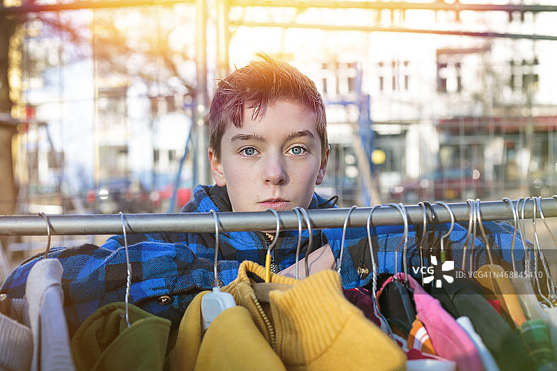一个十几岁的男孩躲在跳蚤市场的衣架后面图片素材