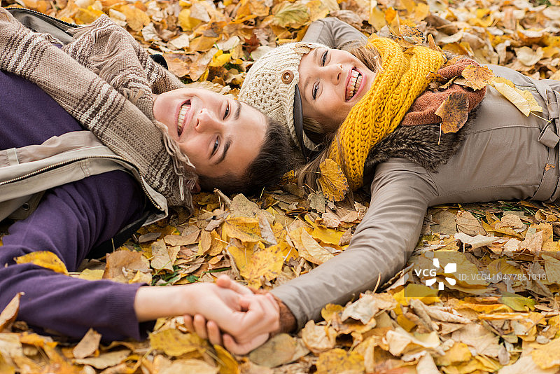 一对快乐的夫妇躺在树叶中看着镜头。图片素材