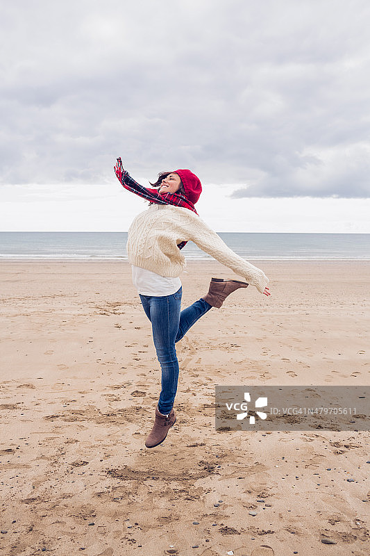 穿着时髦暖和的衣服在海滩上跳来跳去的女人图片素材