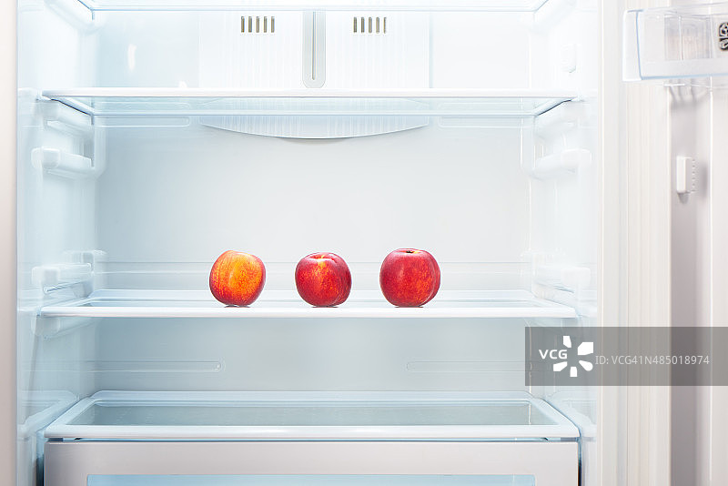 打开冰箱的架子上放着三个橘子和红桃子图片素材