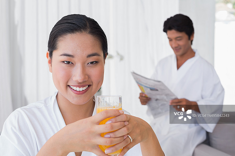 穿着浴袍的女人喝着橙汁，男友在后面图片素材