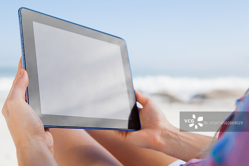 一个女人坐在沙滩上的躺椅上用着平板电脑图片素材