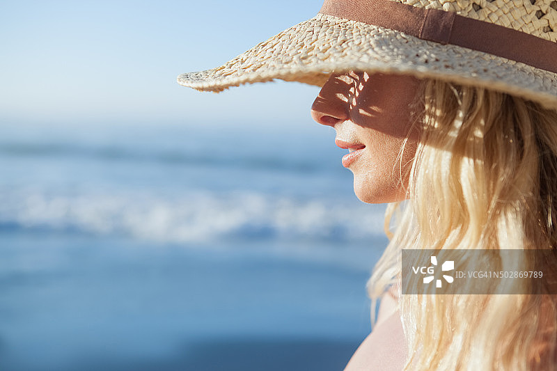 戴着草帽的金发美女在海滩上微笑图片素材