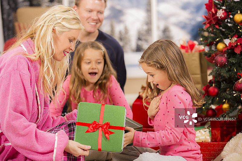 女孩和妈妈一起打开圣诞礼物。树。节日的早晨。家庭。图片素材