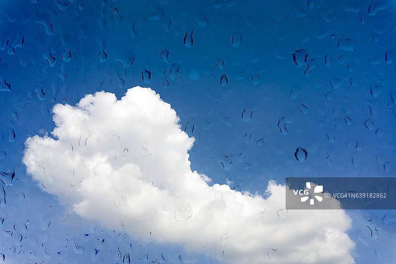 水滴落在蓝色的天空上的玻璃窗上。图片素材