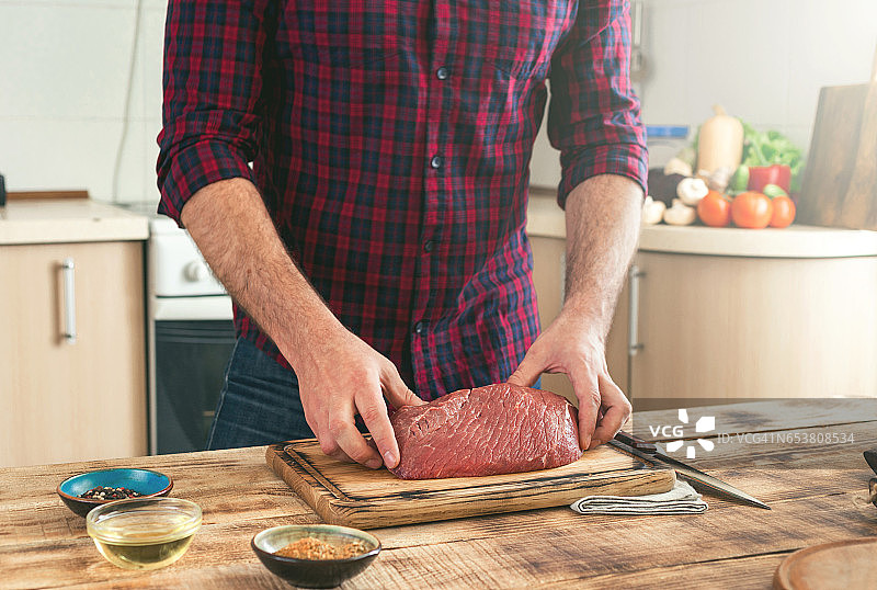 在家庭厨房的木桌上，一个男人拿着一块新鲜的牛肉图片素材