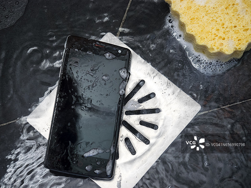智能手机掉在浴室的地板上，旁边是有水的排水管图片素材