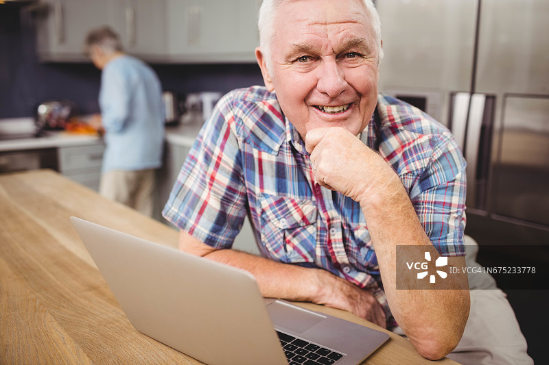 一个快乐的老人在用笔记本电脑，一个女人在厨房工作图片素材