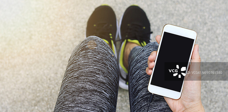 慢跑者使用智能手机，女性跑步者在休息时拿着手机。图片素材