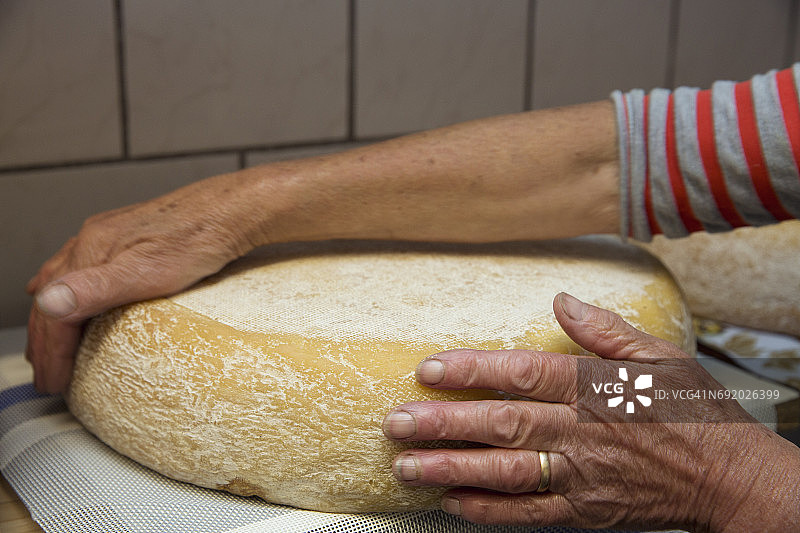 奥地利蒂罗尔，萨特尔伯加尔姆，一名女奶农在厨房里翻整块奶酪图片素材