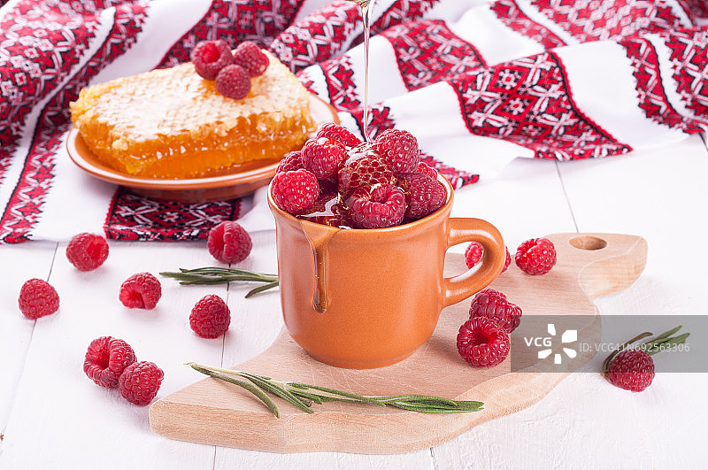 新鲜的覆盆子放在碗里，蜂蜜和迷迭香放在木背景上。夏日浆果。餐巾上的盘子上有覆盆子和蜂窝。乌克兰的风格图片素材