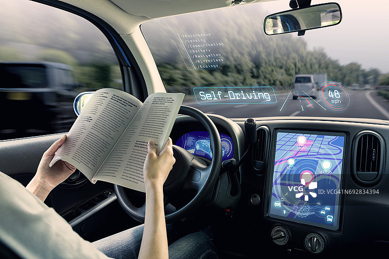 自动驾驶汽车的座舱。一辆车辆运行自动驾驶模式和一个女人驾驶阅读书籍。图片素材