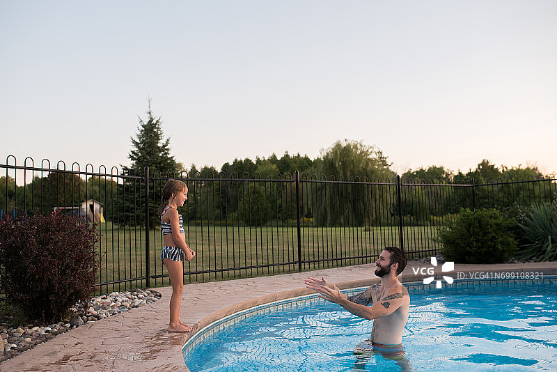 小女孩站在游泳池边上，爸爸在泳池里鼓励她跳下去图片素材