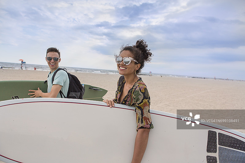 在美国纽约州洛克威海滩，一对年轻夫妇背着冲浪板。图片素材