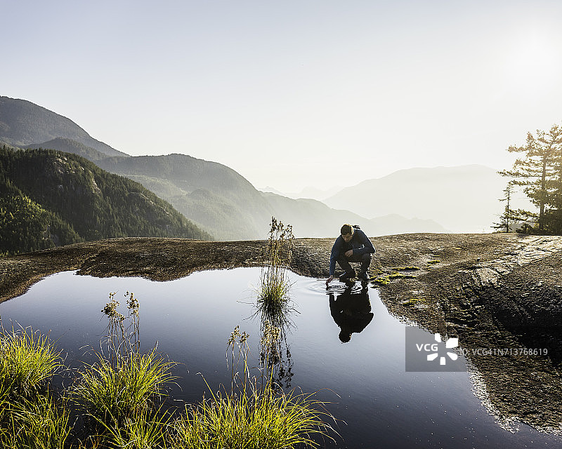 加拿大，不列颠哥伦比亚省，斯夸米什，一名男子在湖中触摸水，俯瞰豪湾湾图片素材