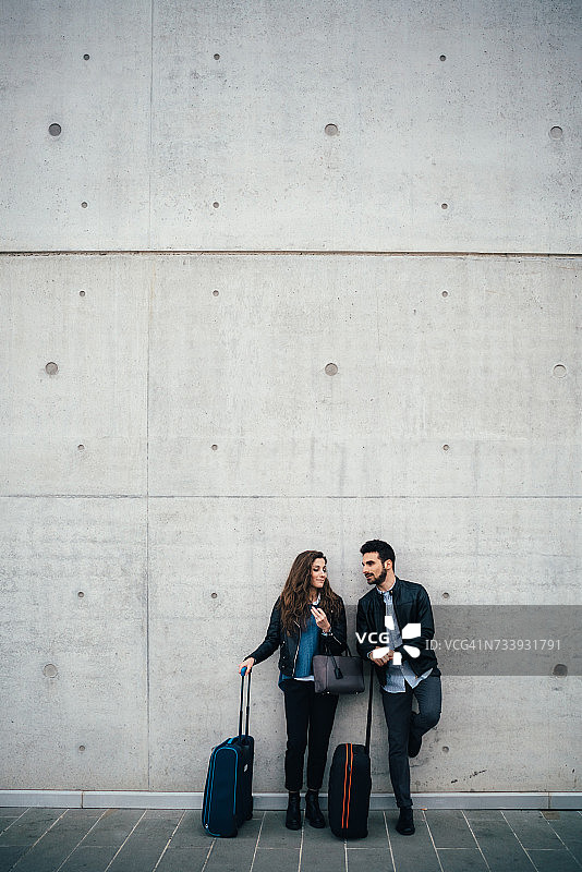 一对夫妇带着行李，灰色墙壁背景，意大利佛罗伦萨图片素材