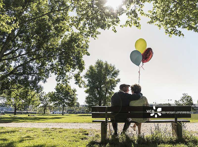 一对快乐的老夫妇拿着气球坐在公园的长椅上图片素材