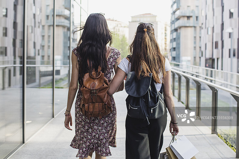 两个背着背包和购物袋的年轻女人走在城市里图片素材
