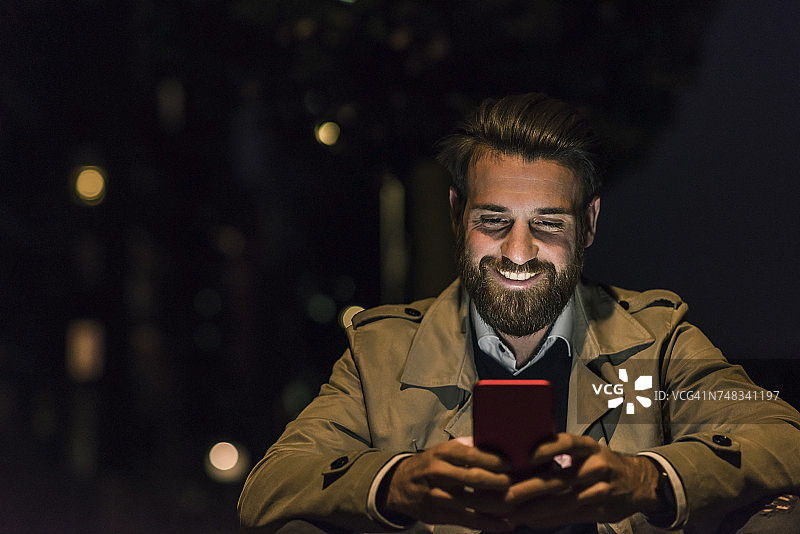 微笑的年轻人在城市的夜晚用手机图片素材