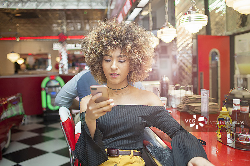 一个年轻女人坐在餐厅里，看着智能手机图片素材