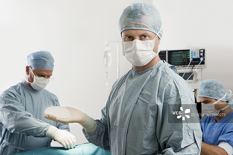 外科医生在手术室里举着乳房植入物的肖像图片素材
