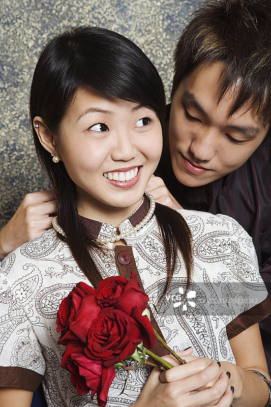 一个年轻男子把一条项链系在一个年轻女子的脖子上的特写图片素材