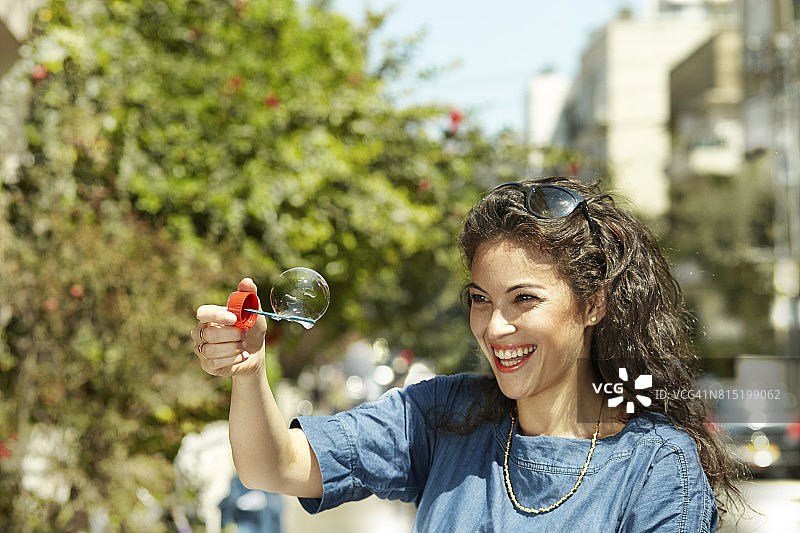 有吸引力的年轻女子笑着玩泡沫在人行道上在一个炎热的阳光灿烂的日子图片素材