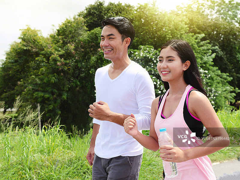 一对年轻幸福的情侣在绿色的背景下奔跑在路上。运动、健身、健康理念。图片素材