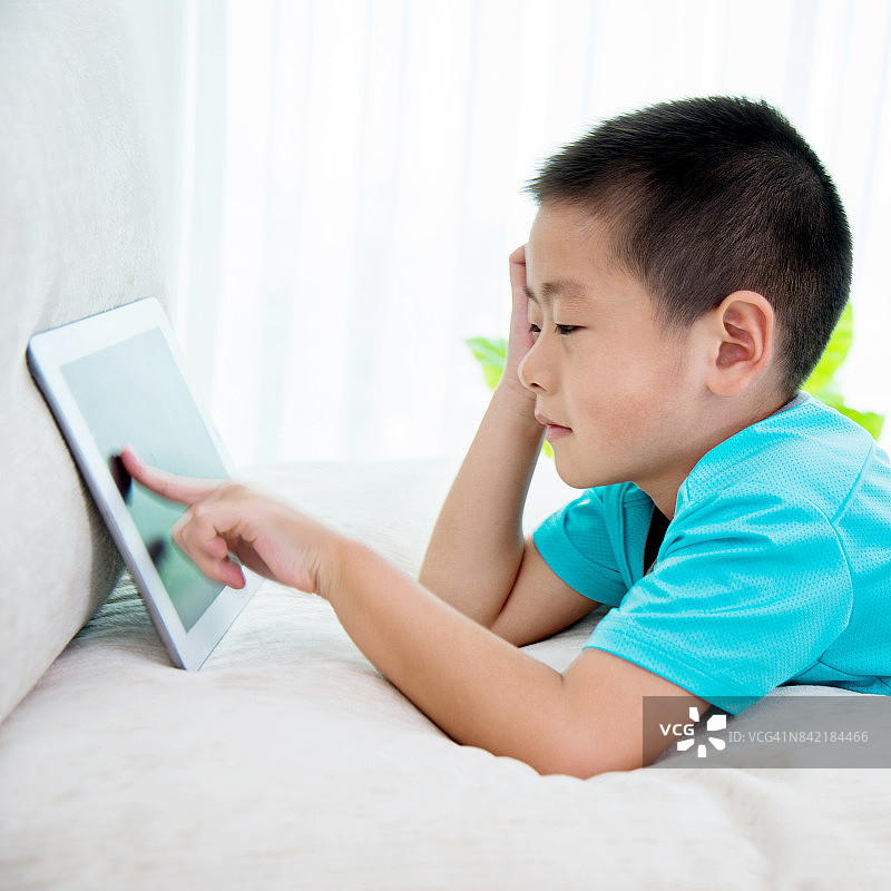 小男孩在沙发上玩数码平板电脑图片素材