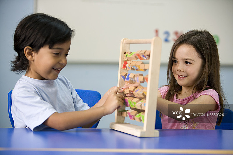 一个小女孩和一个小男孩在教室里玩算盘。图片素材