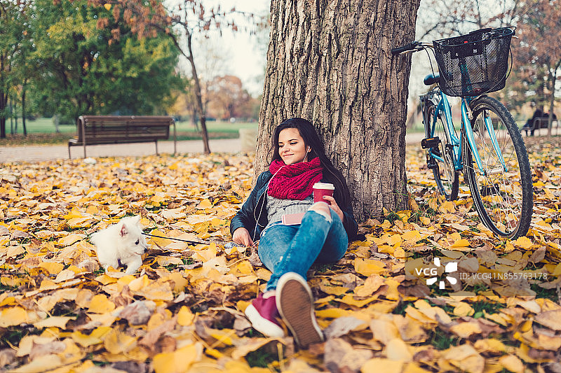 一个十几岁的女孩和她的狗在秋季公园听播客图片素材