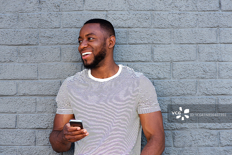 微笑的男人拿着手机靠在灰色的墙上图片素材
