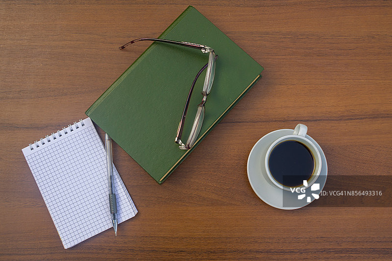 一杯咖啡，书，记事本，笔和眼镜放在木桌上图片素材