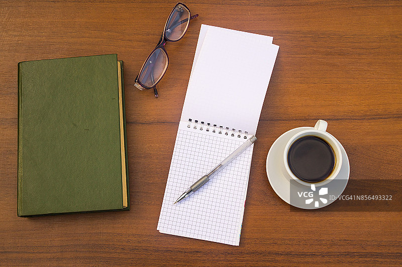 一杯咖啡，书，记事本，笔和眼镜放在木桌上图片素材