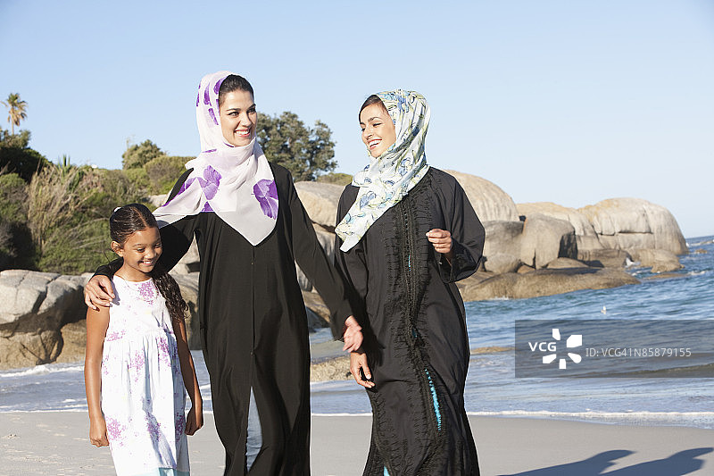两个阿拉伯女人和一个女孩在海滩上散步。图片素材