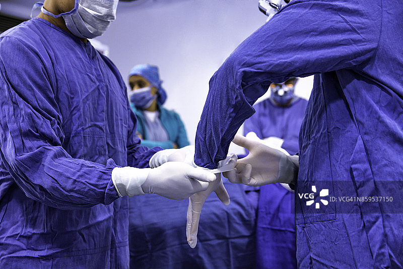 特写外科医生准备手术程序。助手帮助设置手术手套。图片素材