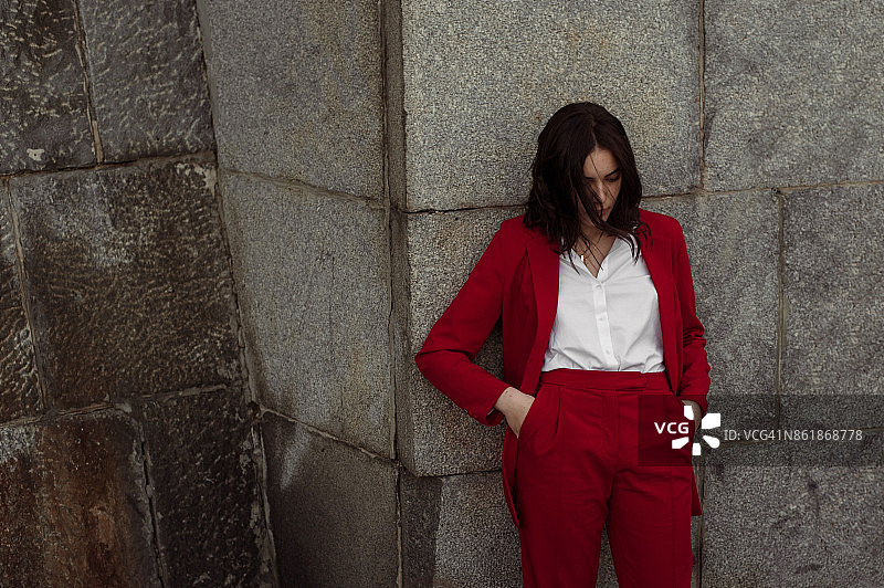 站在砖墙附近的穿着红色长裤套装的女人图片素材