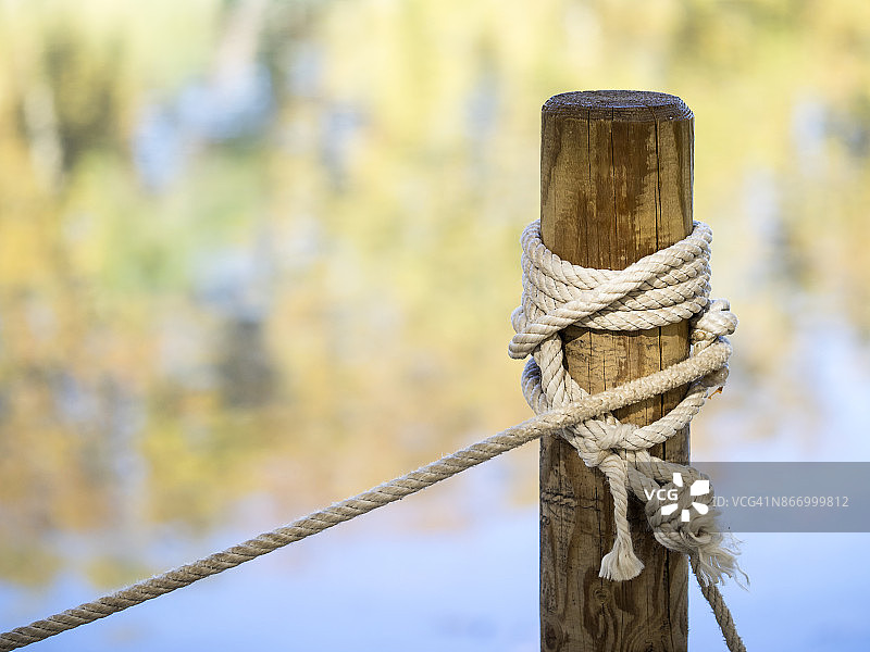 木桩上系着绳子和结，到湖边的一个湖泊与秋天的树叶的颜色的倒影。西班牙图片素材