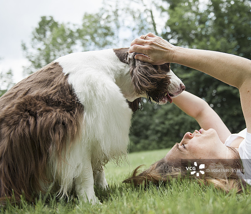 躺在草地上的女人伸出手，狗趴在她身上图片素材