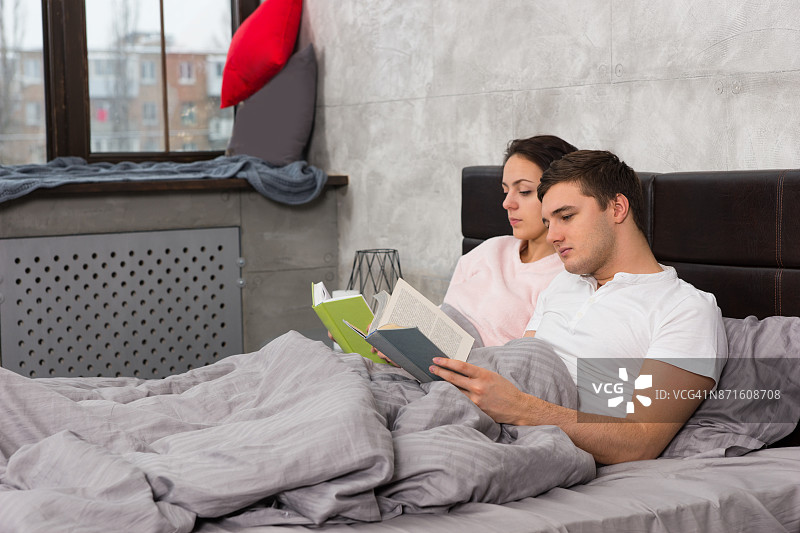 一对年轻的情侣穿着睡衣躺在床上看书图片素材