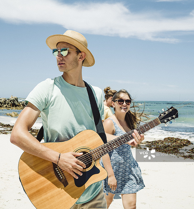 一个年轻人在海滩上给朋友弹吉他图片素材