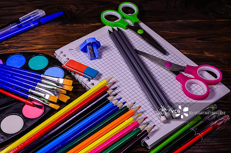一套不同的文具。笔记本，剪刀，铅笔，颜料，画笔放在木桌上。回到学校图片素材